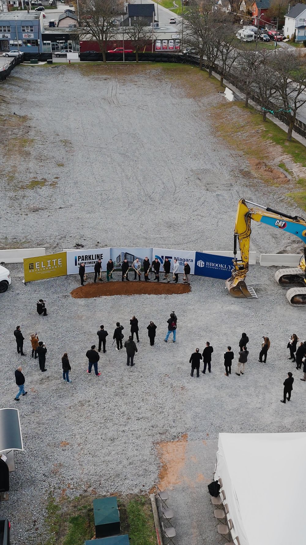 Aerial view of the Parkline Apartments groundbreaking, with guests gathered in a semicircle around the ceremonial soil and excavators on the cleared Park Street site