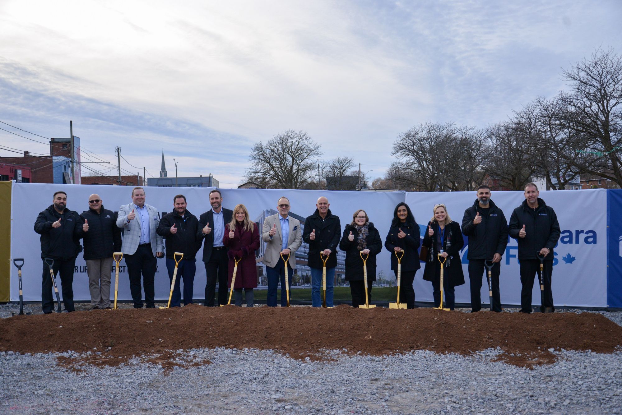 Project partners lined up with gold shovels at a mound of soil during the Parkline Apartments groundbreaking ceremony at 4500 Park Street