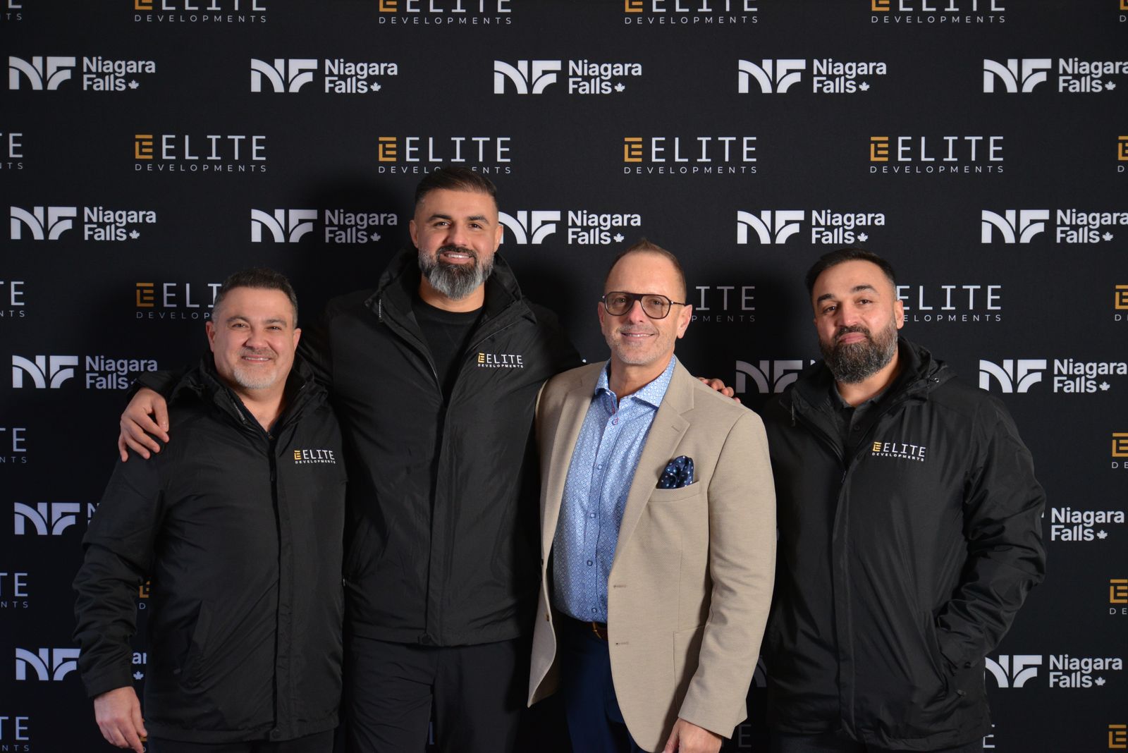 Four project partners standing together in front of the Elite Developments and City of Niagara Falls backdrop at the groundbreaking celebration